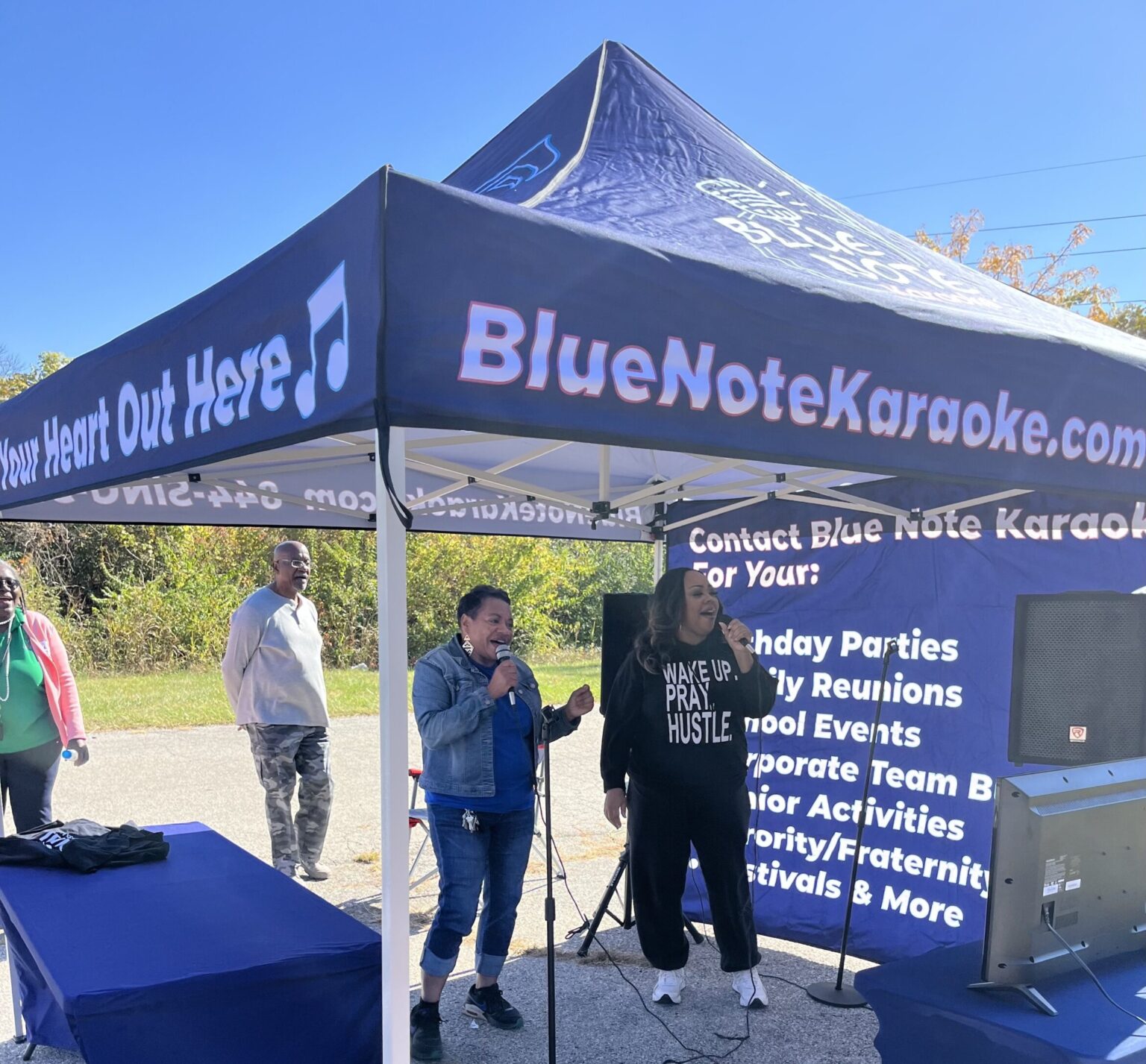 Outdoor karaoke event with a BlueNoteKaraoke.com tent and singers.