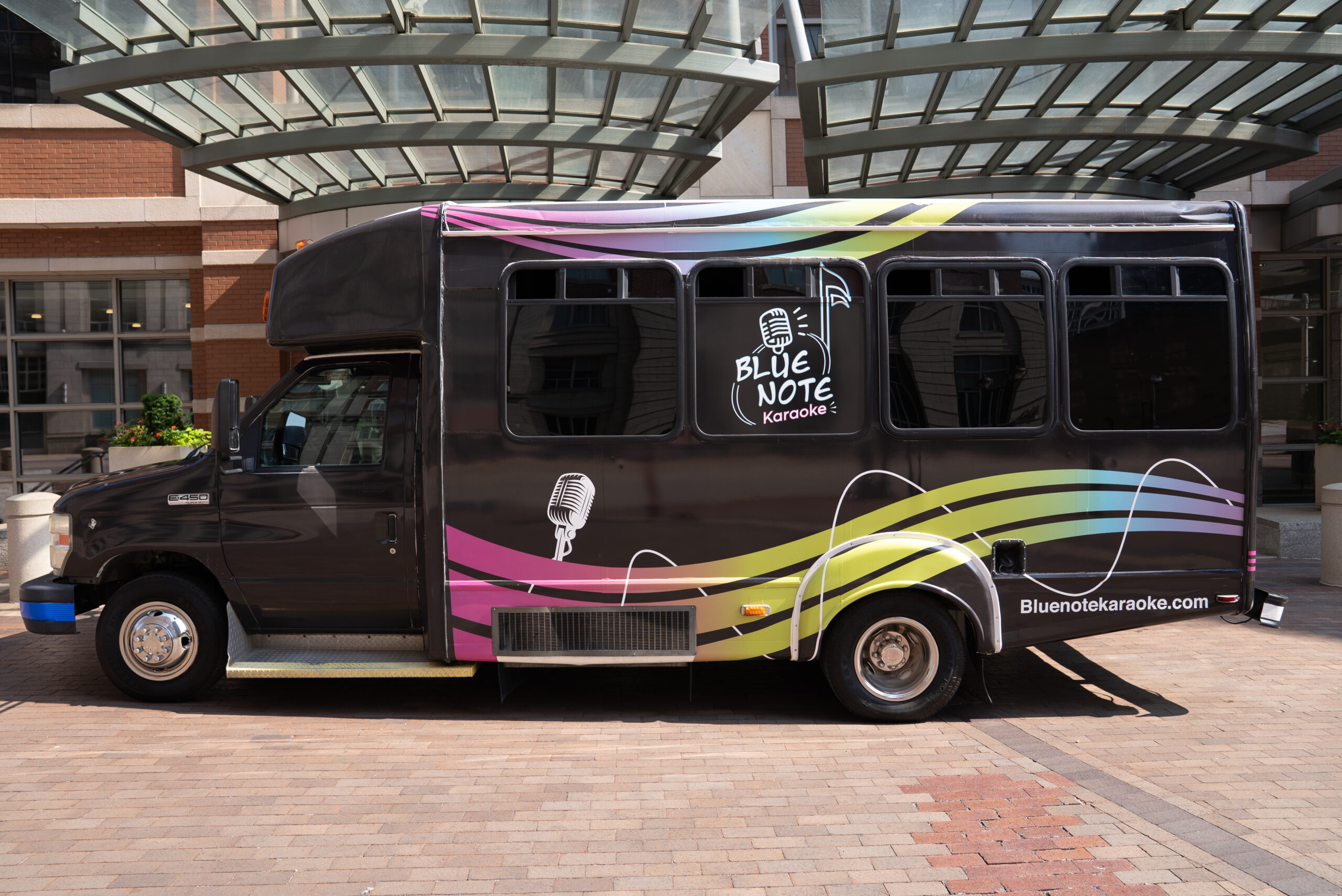 Black bus with colorful wave patterns parked under a glass roof.