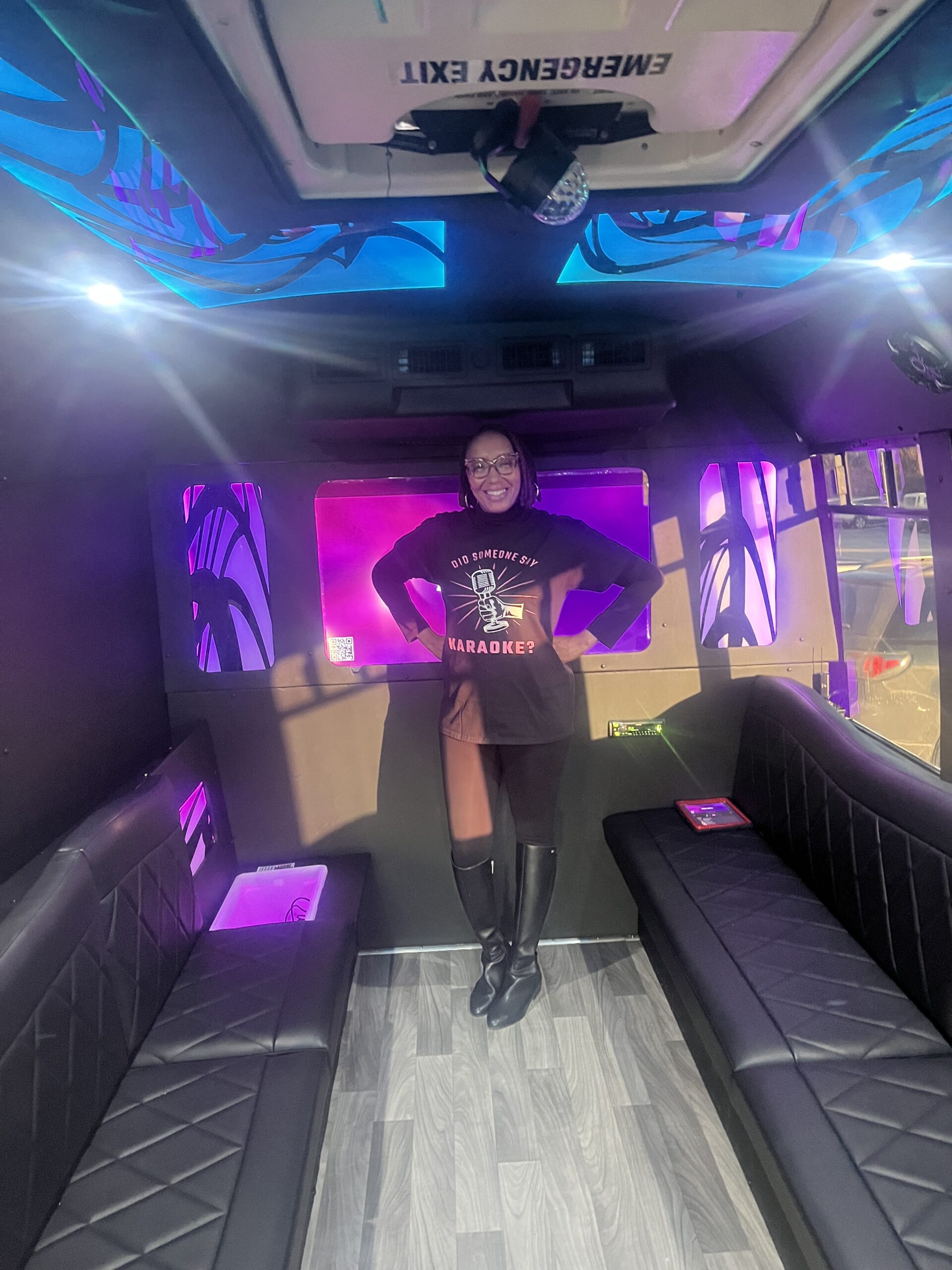 Person standing in a stylish room with purple lighting and black furniture.
