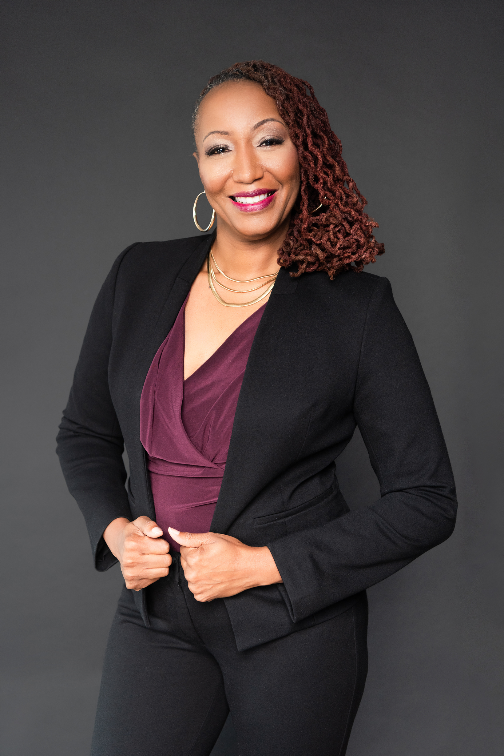 Confident woman in a black blazer and purple top smiles warmly.